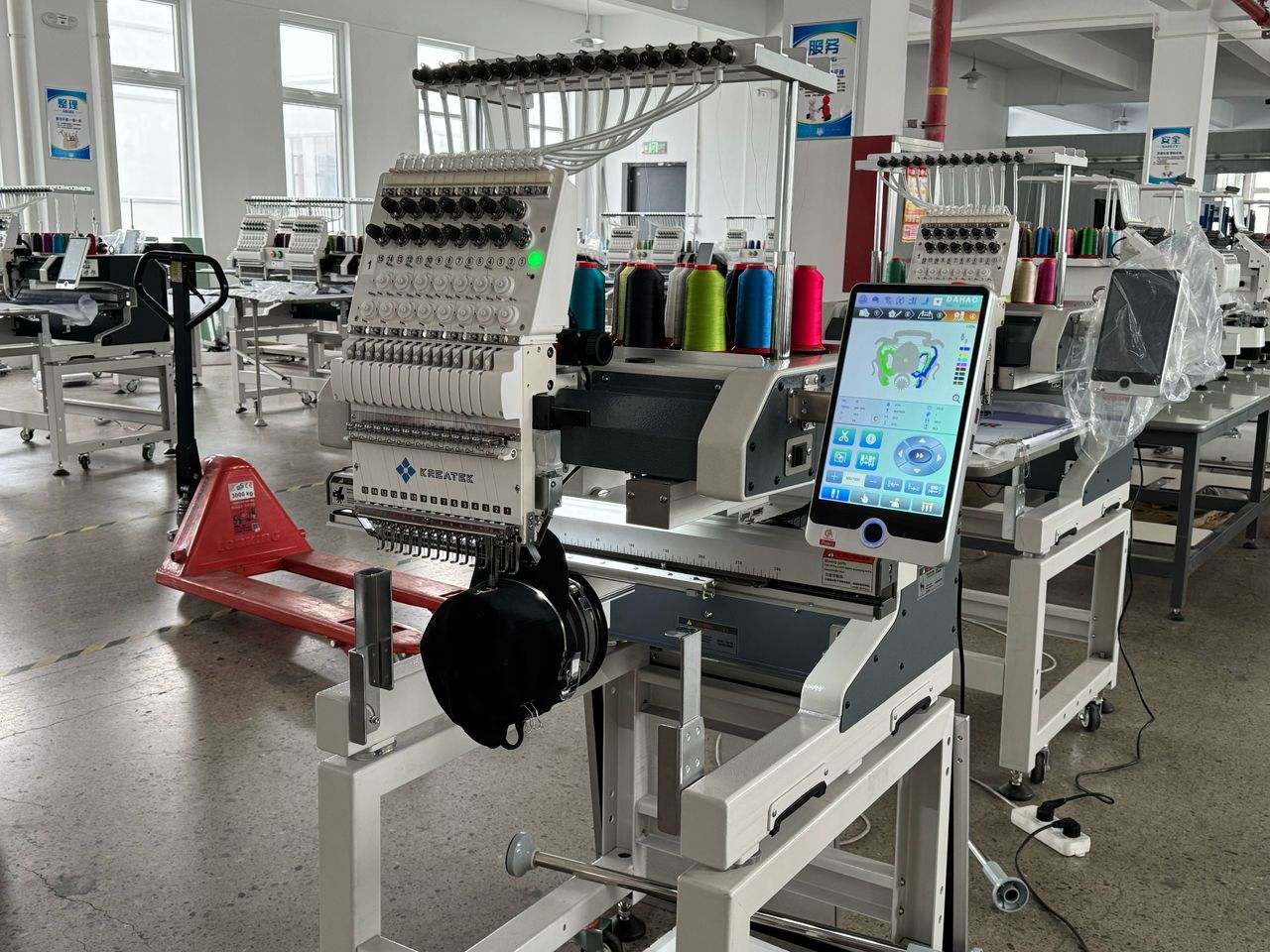 Kreatek BL-1501 industrial embroidery machine with high-speed single head, 12/15 needles, digital touchscreen, and multi-color thread spools in a factory setting.