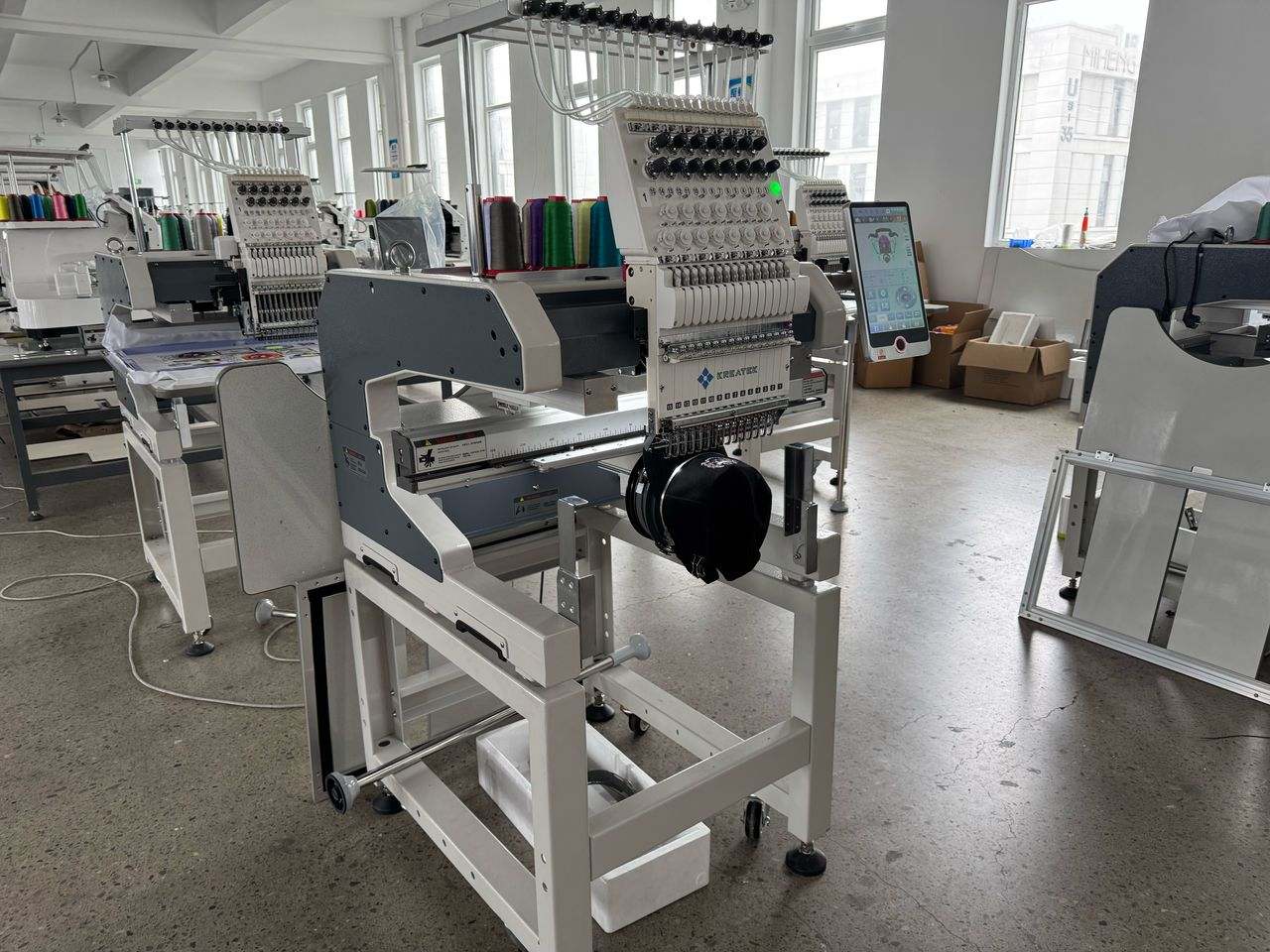 Kreatek III BL-1501 industrial embroidery machine with multi-needle head and touchscreen control in a spacious workshop.
