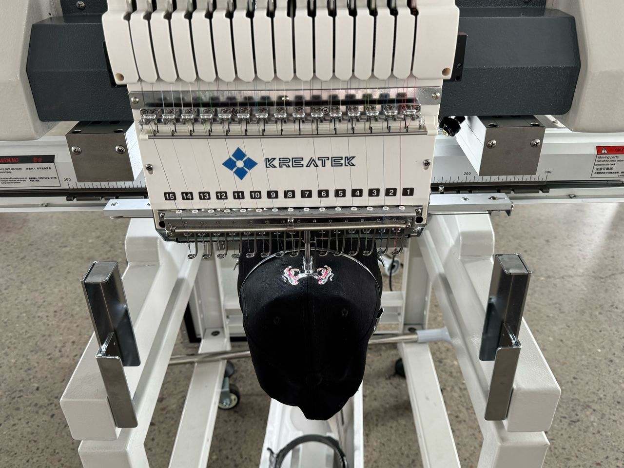 Kreatek BL-1501 industrial embroidery machine stitching a black cap with multiple needles and high-speed precision.