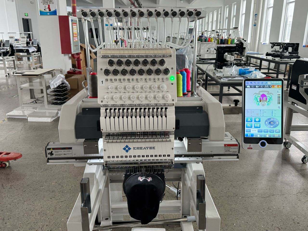 Kreatek III BL-1501 industrial embroidery machine with touchscreen control, multi-needle head, and cap embroidery setup in factory setting